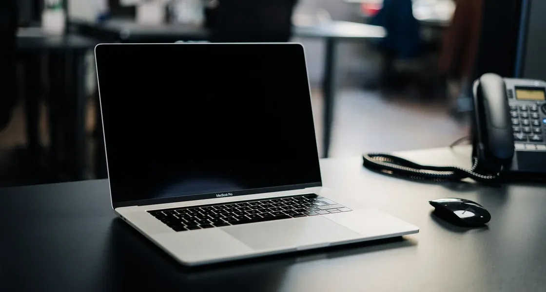 Laptop on an office desk next to a mouse and a desk phone